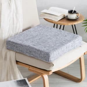 Coussin fauteuil rotin carré et épais posé sur une chaise avec une petite table en fond et un livre avec une tasse posé dessus