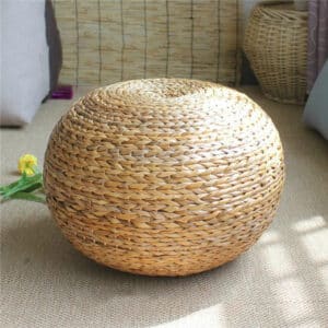 Pouf rotin style naturel et épuré sur le sol avec une fleur à gauche et de la décoration en fond